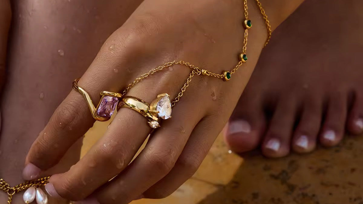 Close-up of a hand wearing gold jewelry with gemstones on a sandy background
